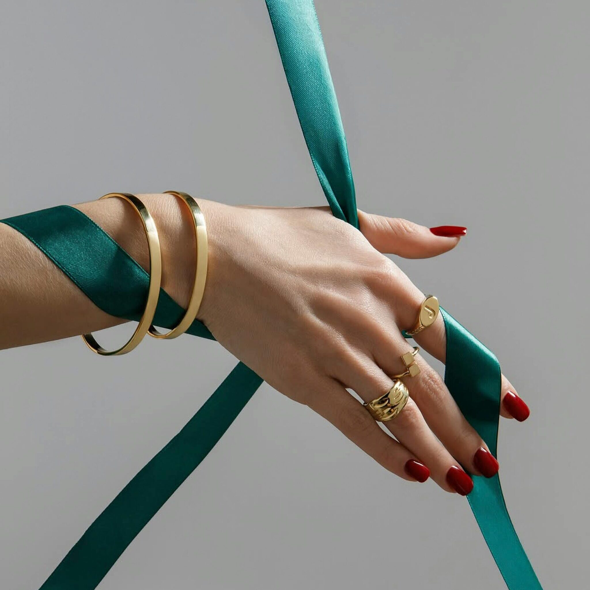 Close-up of elegant hands with gold jewelry and teal ribbon against a neutral background.