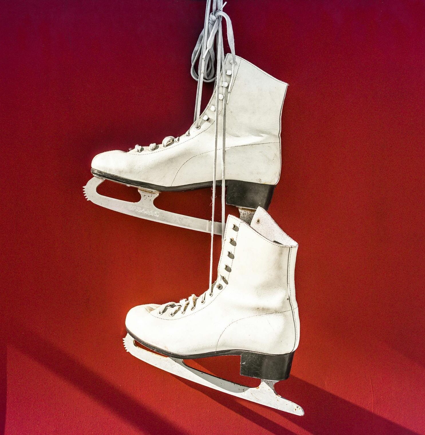 Pair of white ice skates hanging on a vibrant red wall, perfect for winter sports imagery.