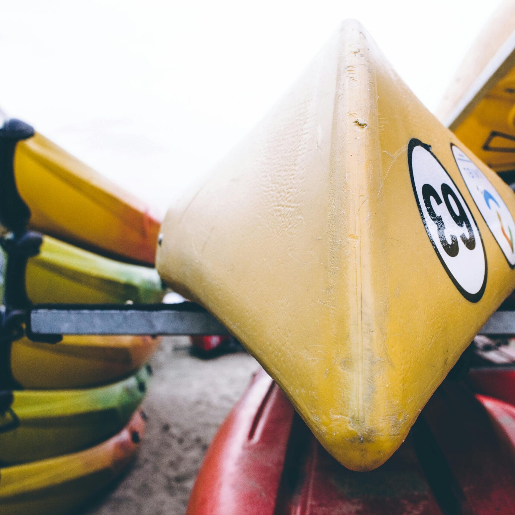 A detailed view of brightly colored kayaks stacked outdoors, focusing on a yellow kayak with numbers.