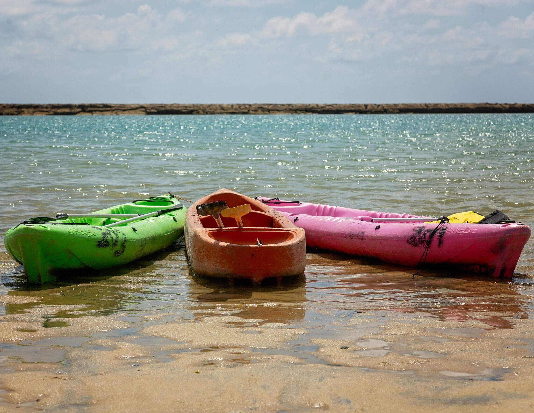 Three vibrant kayaks rest on a sunlit beach, inviting a day of adventure.