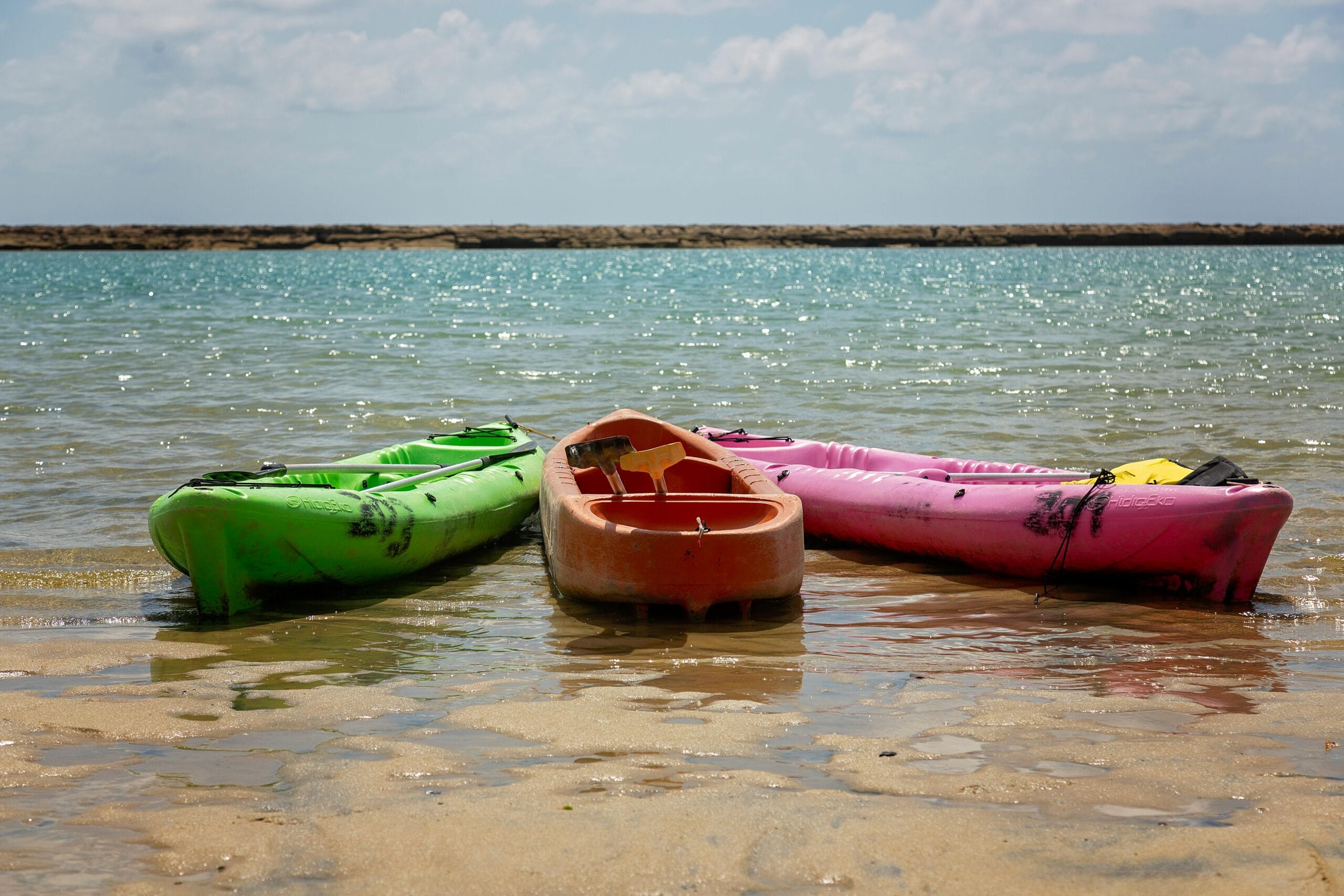 Three vibrant kayaks rest on a sunlit beach, inviting a day of adventure.