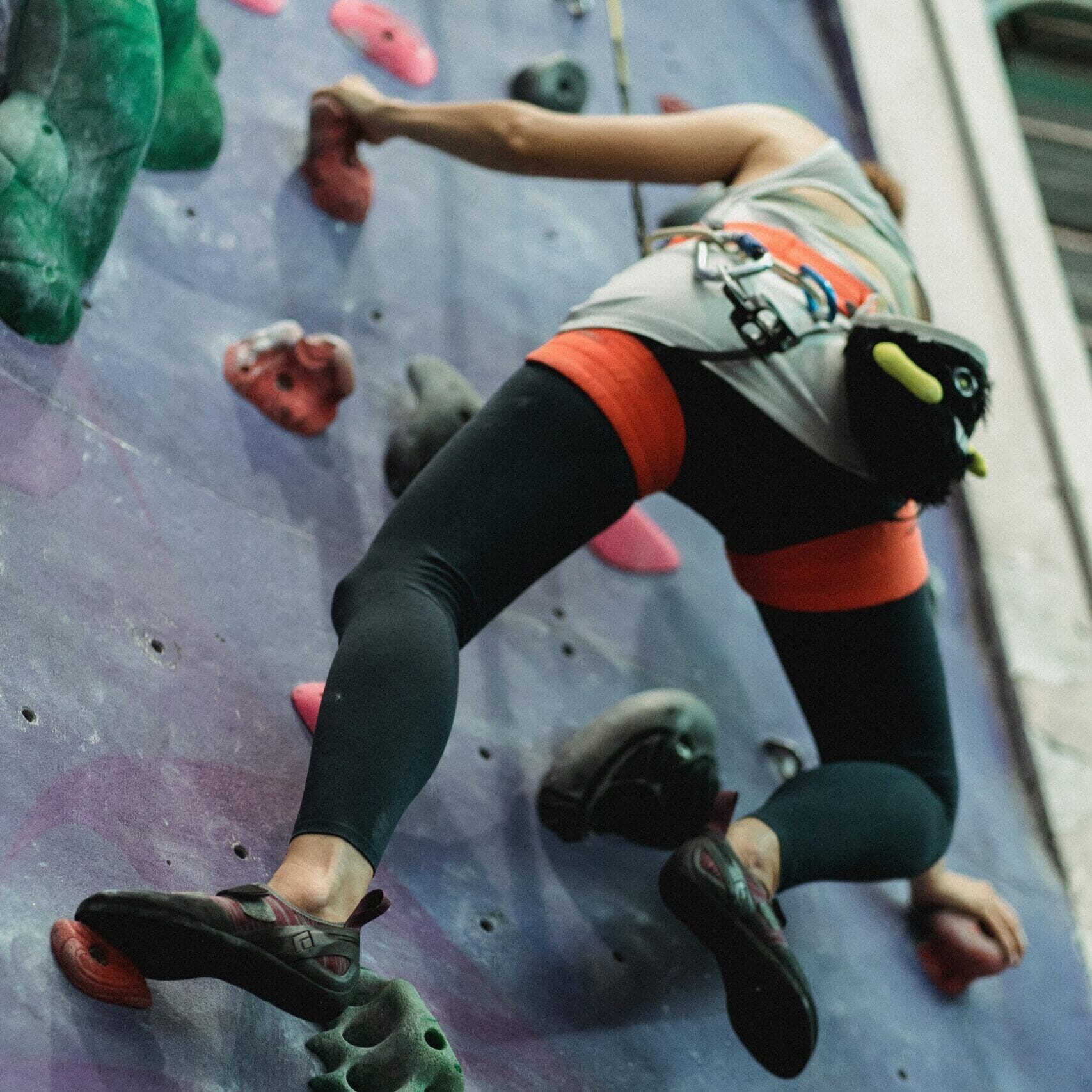 From below of unrecognizable young strong female mountaineer in sportswear and protective gear climbing wall in bouldering center