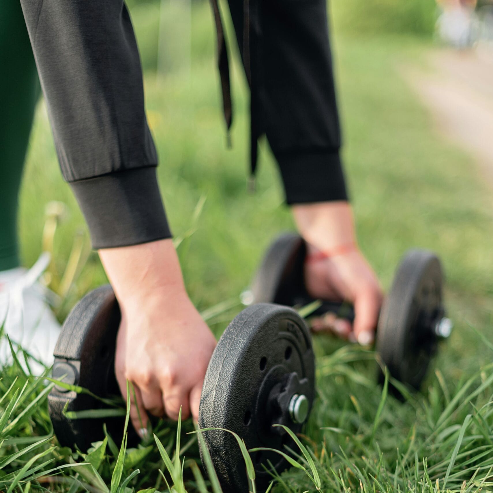 A person lifting dumbbells outdoors on grass, promoting fitness and healthy lifestyle.