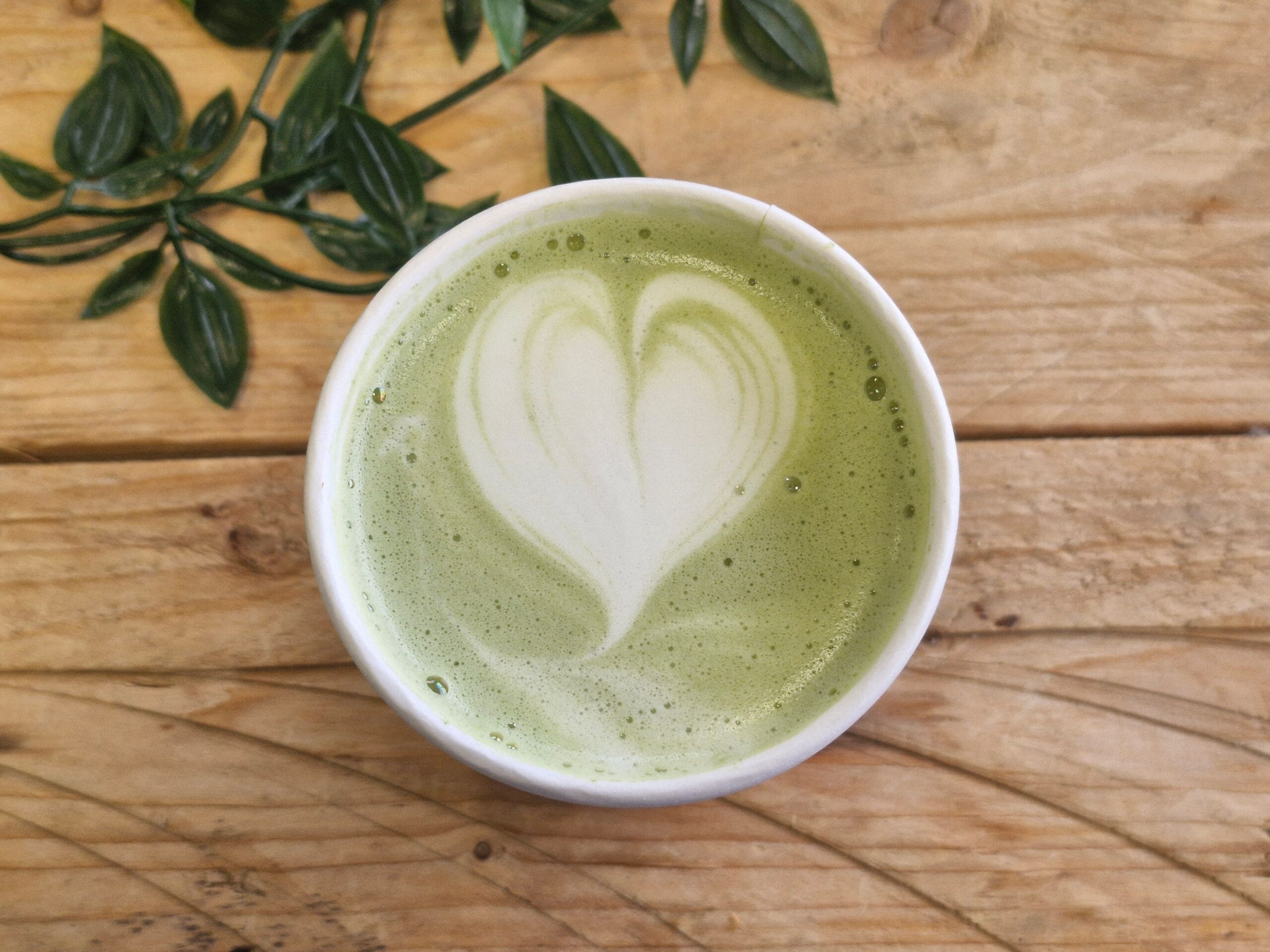 Aesthetic matcha green tea with heart latte art in a cup on wooden table.
