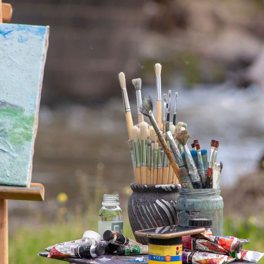 Art materials including brushes, canvas, and paints by a riverside, ideal for creative inspiration.